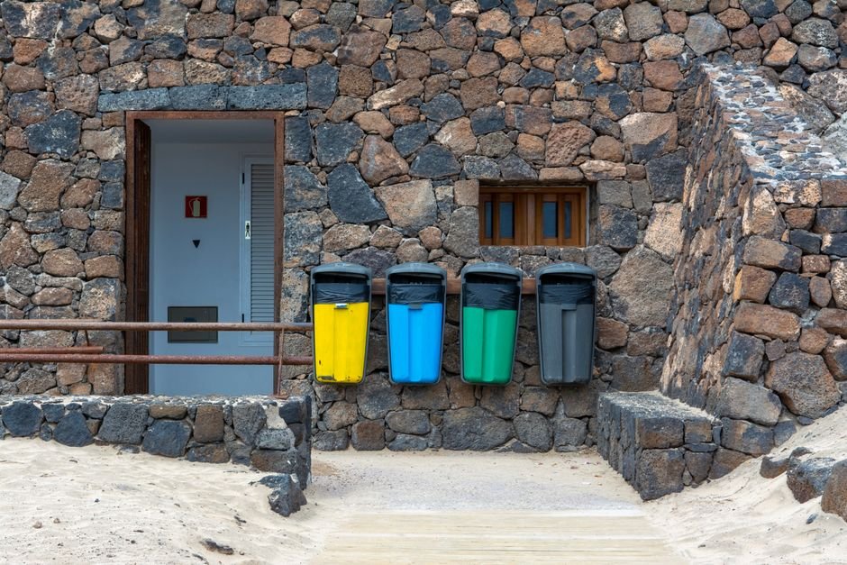 Poubelles de tri colorées alignées contre un mur en pierre, sans cache poubelle en bois