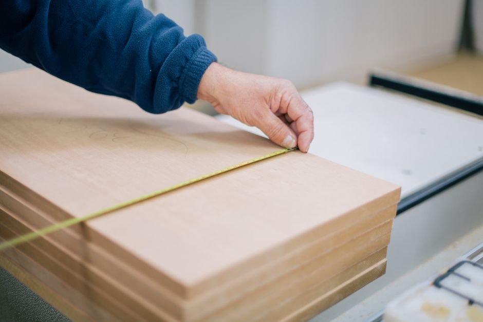 Prise de mesure au mètre ruban sur une planche de bois avant de fabriquer un cache poubelle en bois